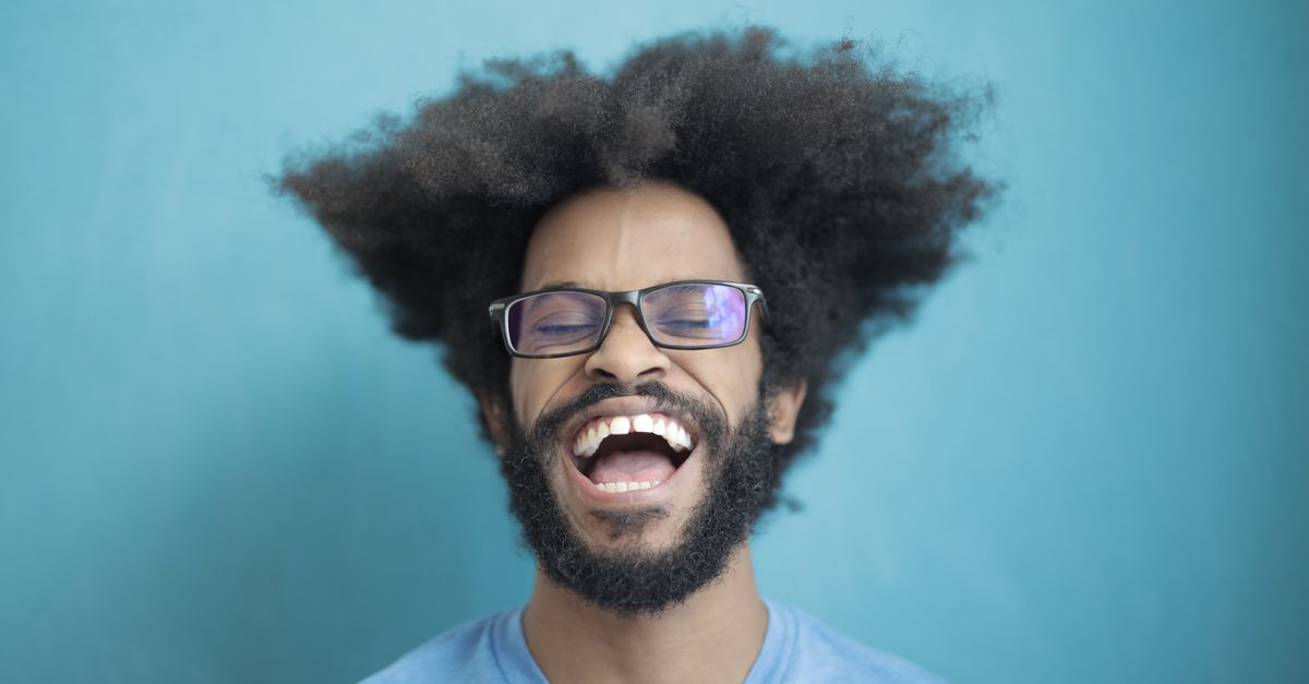 Happy man with afro hair and glasses laughing joyfully against a blue background.